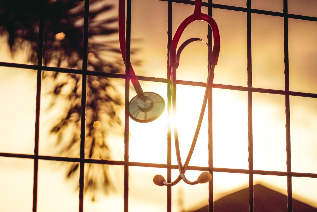 red stethoscope hanging from a metal fence backlit by the sun